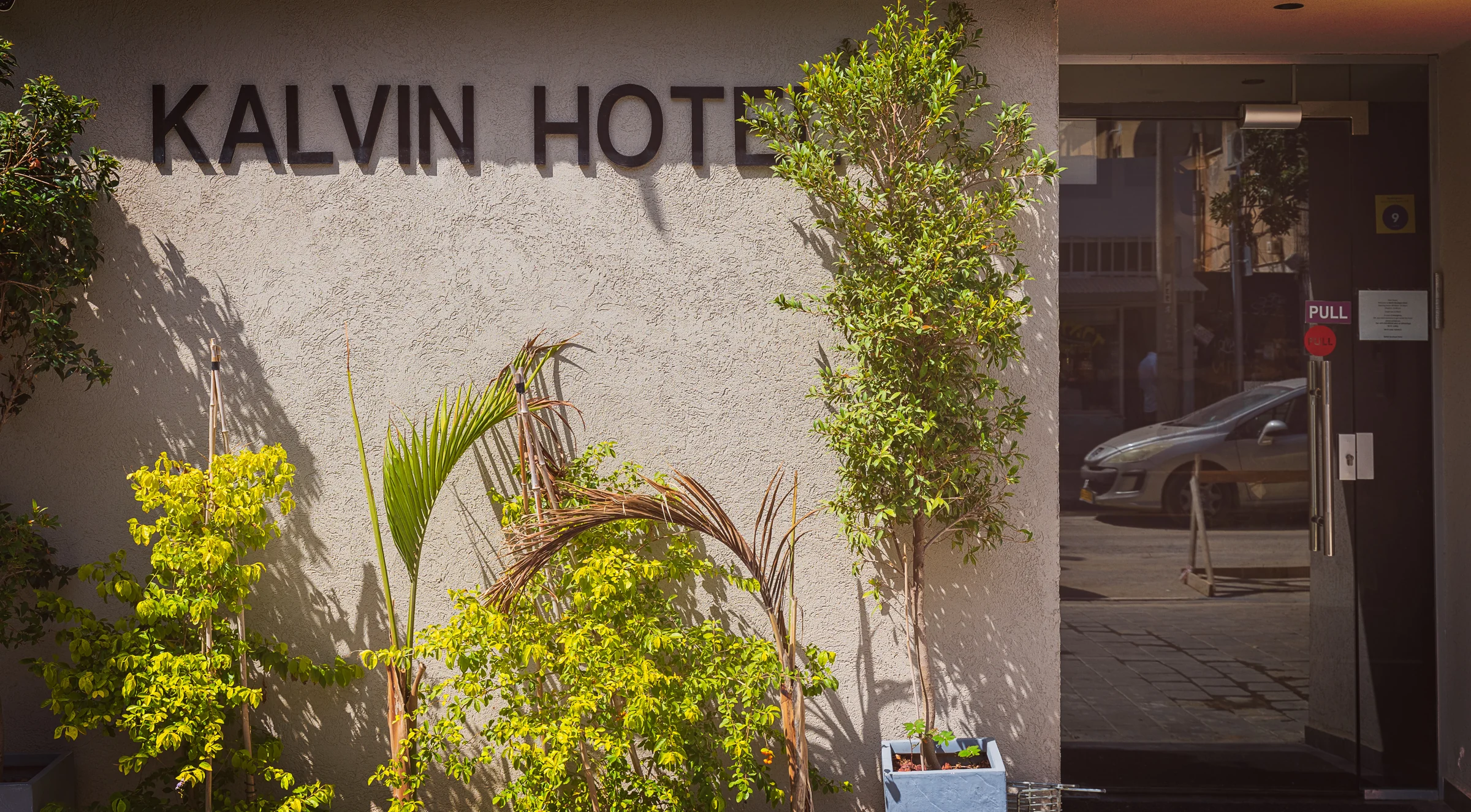 The entrance to Kalvin Boutique Hotel on a Tel Aviv street, framed by greenery.